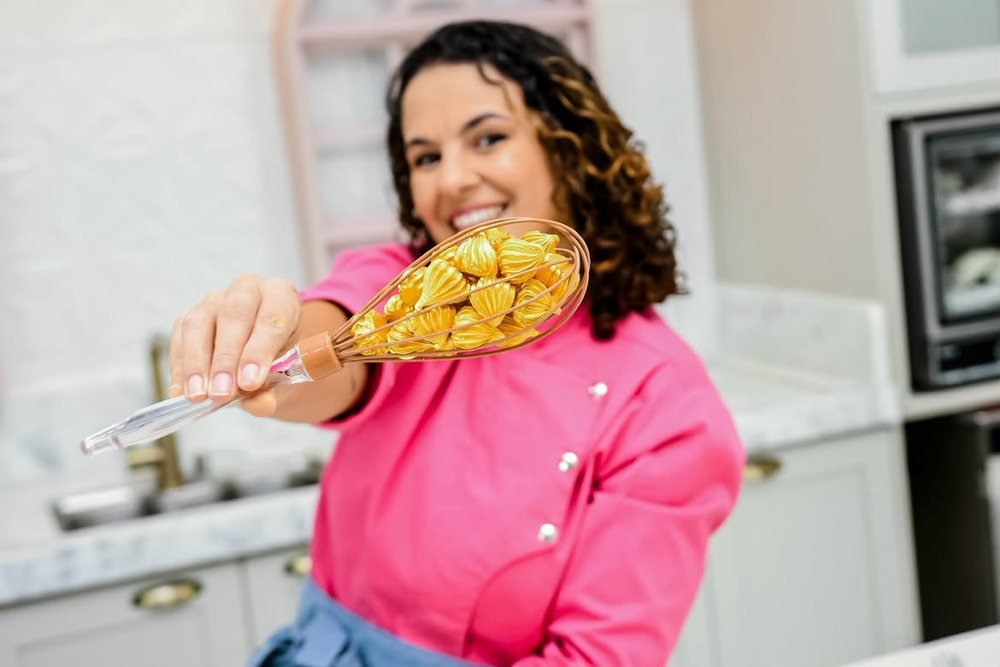 Camila sorrindo, segurando uma colher com suspiros caramelizados
